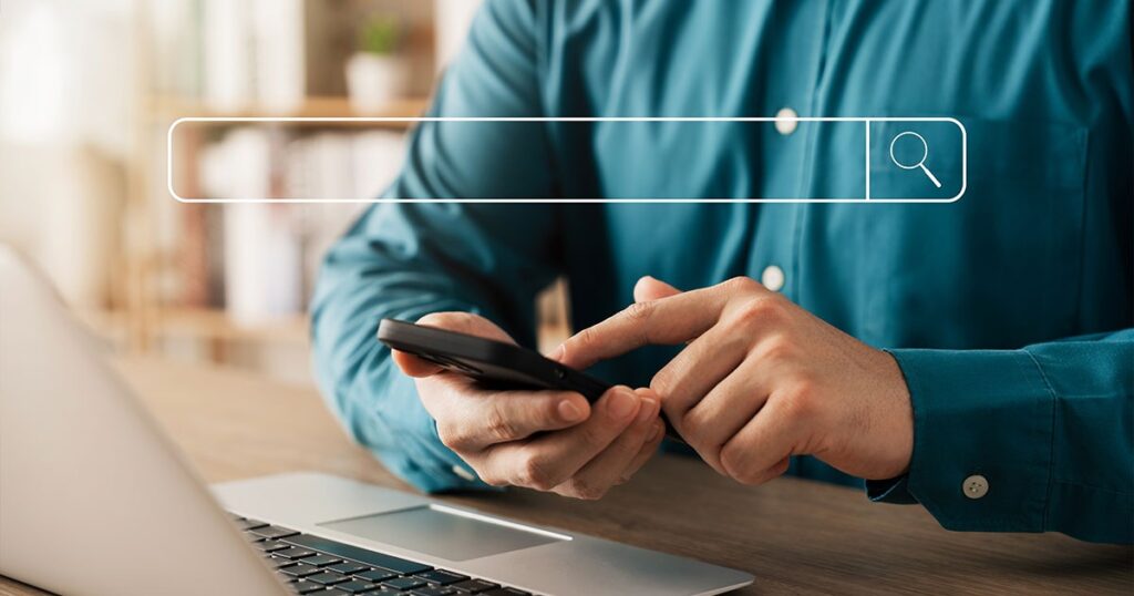 Person using smartphone and laptop with search bar overlay, representing search engine optimization (SEO) services.