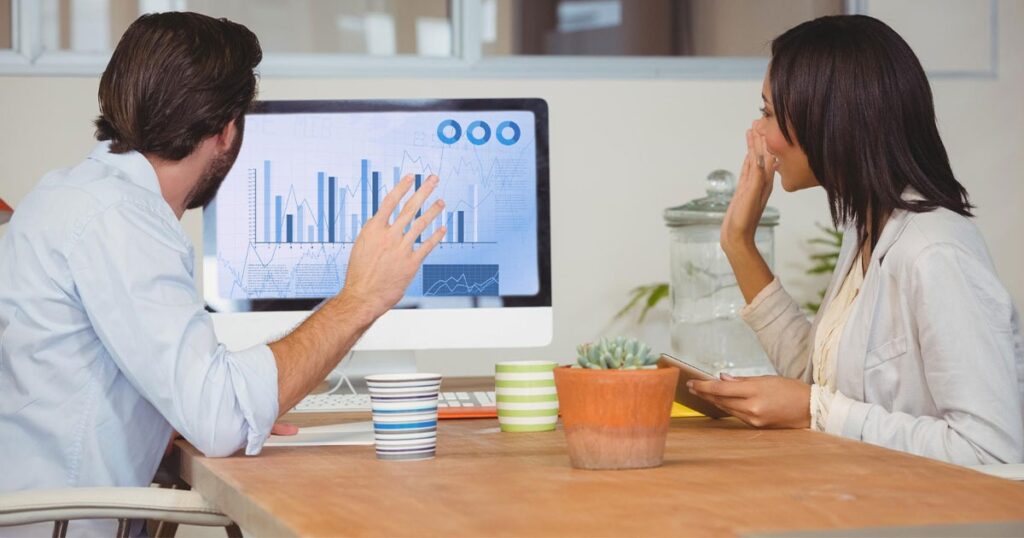 A man and woman collaborate at a desk, focused on a computer screen displaying SEO improvement strategies.