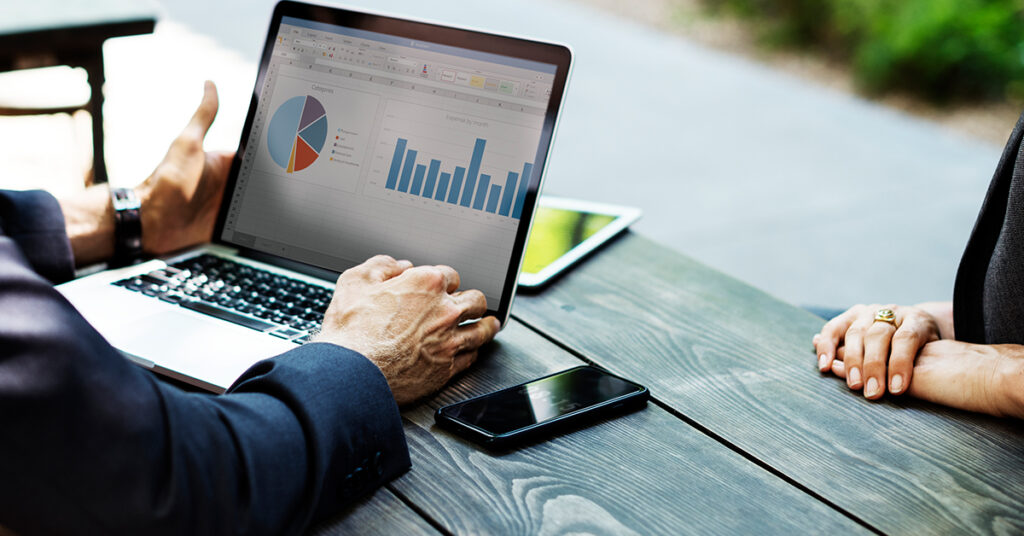 Business professionals reviewing marketing analytics and performance charts on a laptop during an outdoor meeting.