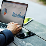 Business professionals reviewing marketing analytics and performance charts on a laptop during an outdoor meeting.